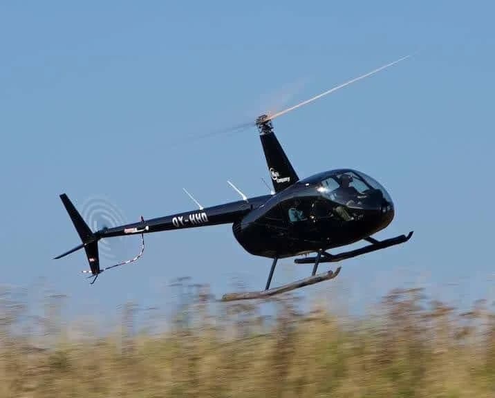 En sort helikopter flyver lavt over græsset