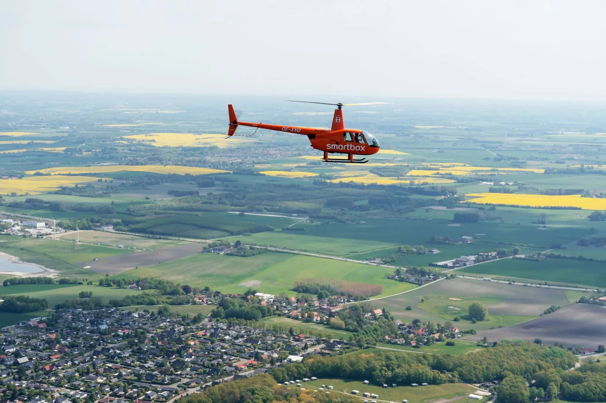 En orange helikopter flyver over marker og en by